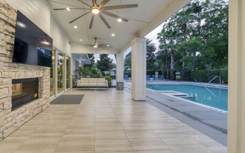 a covered porch with a media area and a pool nearby